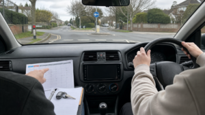 Right-hand-drive UK learner car interior with a two-week driving lesson plan on the dashboard, approaching a quiet residential roundabout.